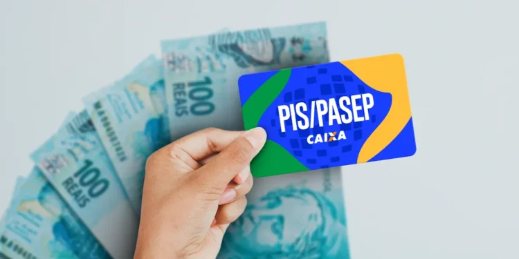 Cartão PIS/PASEP da Caixa sendo manuseado com notas de R$ 100 de fundo, ilustrando a liberação dos novos lotes de pagamento do Abono Salarial.