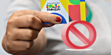 Mão segurando cartão colorido do Programa Bolsa Família com um sinal vermelho de proibição sobreposto.