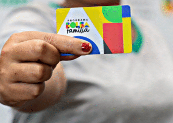 Mão segurando cartão colorido do Programa Bolsa Família com logotipo e design geométrico.