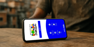 Tela do aplicativo Bolsa Família aberta em um celular sobre uma mesa, mostrando opções de acesso e serviços da Caixa.