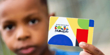 Criança segurando um cartão do Programa Bolsa Família em destaque.