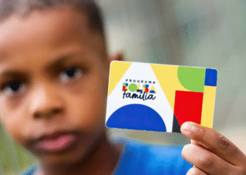Criança segurando cartão do Programa Bolsa Família em close-up, com foco no cartão colorido.