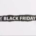 Faixa preta rasgada em papel branco com a inscrição 'Black Friday' e um ícone de carrinho de compras, simbolizando a abertura de ofertas.