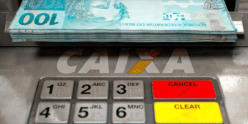 Caixa eletrônico com cédulas de 100 reais saindo do dispenser e teclado numérico em destaque.