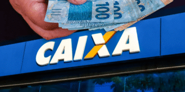 Mão segurando notas de 100 reais acima da fachada de uma agência da CAIXA