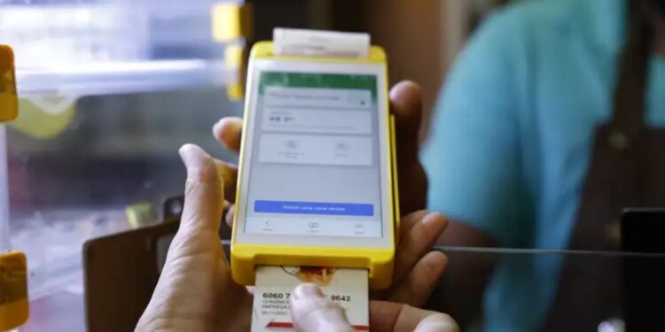 Pessoa segurando máquina de cartão amarela com cartão de crédito sendo inserido para pagamento