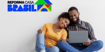 Casal sentado no chão sorrindo enquanto usa notebook, com o logo do programa Reforma Casa Brasil ao fundo.