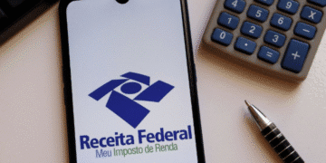 Aplicativo da Receita Federal aberto em celular ao lado de calculadora e caneta.