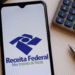 Aplicativo da Receita Federal aberto em celular ao lado de calculadora e caneta.