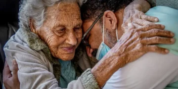 Mulher idosa e homem de óculos com máscara facial se abraçando com carinho e ternura
