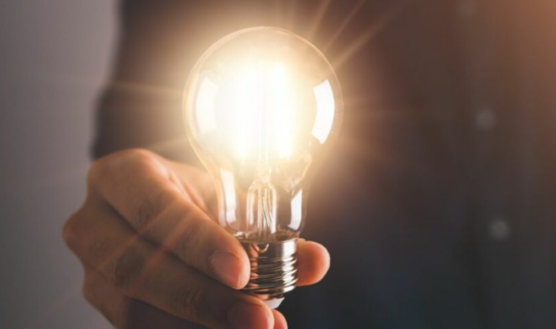 Pessoa segurando uma lâmpada acesa representando o aumento no consumo de energia elétrica.