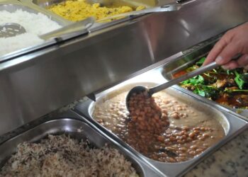 Pessoa servindo-se de feijão em um buffet de restaurante por quilo, ilustrando as novas regras do Governo para o uso do vale-alimentação e vale-refeição.