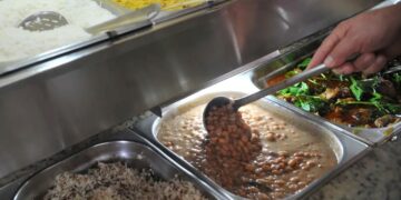 Pessoa servindo-se de feijão em um buffet de restaurante por quilo, ilustrando as novas regras do Governo para o uso do vale-alimentação e vale-refeição.