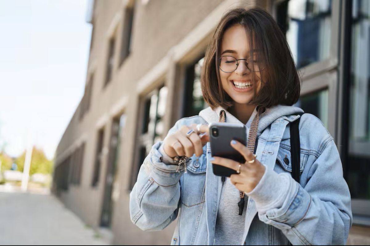 Jovem feliz usando o celular na rua, simbolizando a facilidade e a praticidade de acompanhar e solicitar a renegociação do FIES por meios digitais.