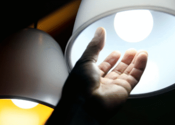 Mão próxima a uma lâmpada acesa representando o aumento no consumo de energia elétrica.