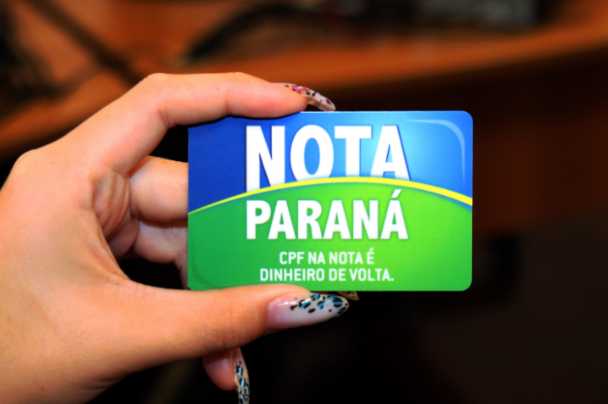 CPF na Nota surpreende com prêmio de R$ 100 mil Pessoa segurando um cartão do programa Nota Paraná com o texto “CPF na nota é dinheiro de volta”.