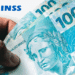 Mão segurando cédulas de 100 reais ao lado do logo do INSS.