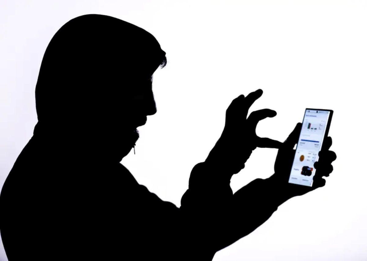 Silhueta de pessoa com capô simulando uma fraude digital em celular