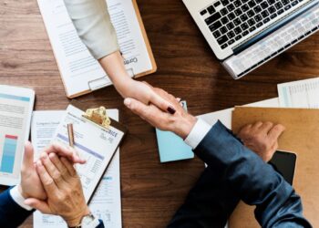 Aperto de mãos sobre uma mesa de reunião com documentos e um laptop, simbolizando o acordo e a conclusão de uma negociação financeira de dívidas bancárias.