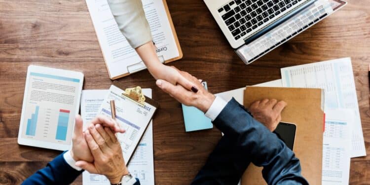 Aperto de mãos sobre uma mesa de reunião com documentos e um laptop, simbolizando o acordo e a conclusão de uma negociação financeira de dívidas bancárias.