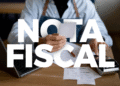 Pessoa segurando uma nota fiscal sobre a mesa, com a frase “Nota Fiscal” em destaque.