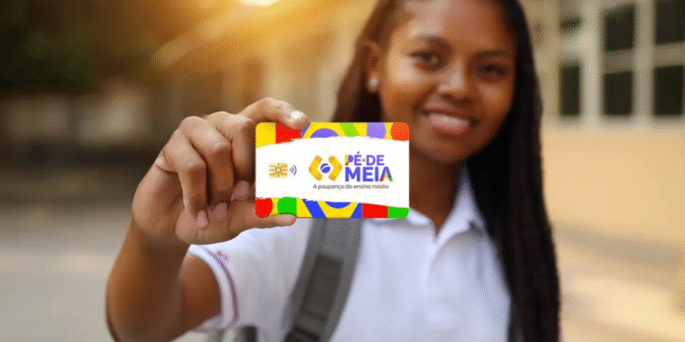 Estudante sorridente segurando o cartão colorido do programa Pé-de-Meia, com logotipo e texto "A poupança do ensino médio", em fundo desfocado de ambiente escolar ao entardecer.