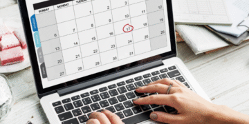 Laptop exibindo calendário digital com o dia 17 circulado em vermelho, ao lado de agenda física, destacando planejamento para o feriado de 15 de novembro.
