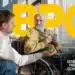 Homem ajudando idoso em cadeira de rodas segurando copo de água, ilustrando o benefício BPC