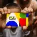 Mãos segurando um cartão colorido com design do Programa Bolsa Família em destaque.