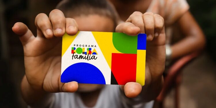 Criança segurando cartão do Programa Bolsa Família colorido em foco com adulto ao fundo