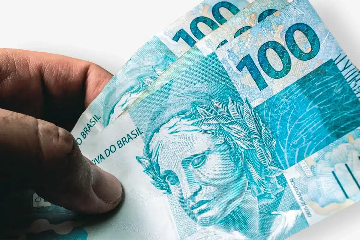 Notas de 100 reais e o impacto do INPC e PIB no salário mínimo Notas de 100 reais sendo seguradas, ilustrando a relação entre INPC, PIB e o cálculo do salário mínimo no Brasil.