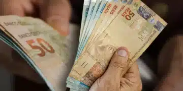 Mão segurando cédulas de reais, simbolizando o pagamento da segunda parcela do 13º salário.