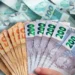Mão segurando várias cédulas de 50 e 200 reais com outras notas de 100 reais ao fundo