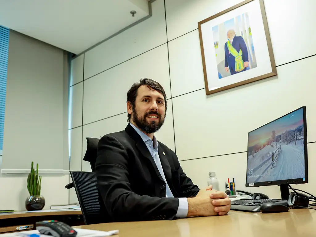 Homem de terno sentado em escritório moderno Homem sorridente de terno preto sentado em cadeira diante de mesa com computador em escritório.