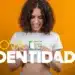 Mulher jovem sorridente segurando a Nova Carteira de Identidade Nacional (CIN) em frente ao corpo, com fundo amarelo vibrante.
