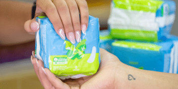Duas pessoas trocando um pacote de absorventes higiênicos, ilustrando o Programa Dignidade Menstrual do Governo Federal, que permite a retirada gratuita de absorventes no SUS.