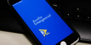 Tela de celular mostrando o aplicativo Auxílio Emergencial em fundo azul sobre teclado.