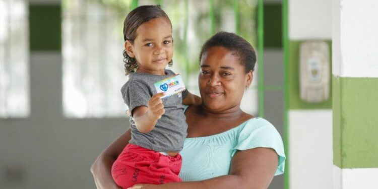 Mãe segurando uma criança que exibe o cartão do programa Mães de Pernambuco.