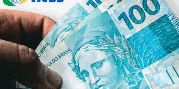 Mão segurando notas de 100 reais com logo do INSS ao fundo, ilustrando saque de benefícios.