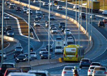 Trânsito movimentado com carros, motos e ônibus em uma estrada urbana, representando a dinâmica de transportes nas cidades.