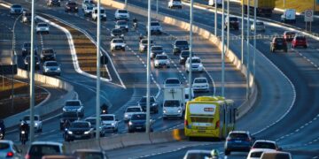 Trânsito movimentado com carros, motos e ônibus em uma estrada urbana, representando a dinâmica de transportes nas cidades.
