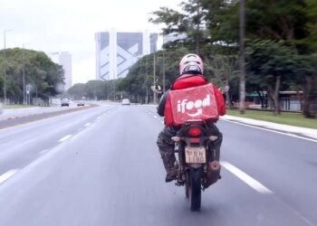 Entregador do iFood pilotando moto em via urbana, simbolizando o trabalho da plataforma e o recebimento de um bônus de incentivo que pode variar entre R$ 900 e R$ 3 mil.
