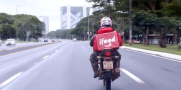 Entregador do iFood pilotando moto em via urbana, simbolizando o trabalho da plataforma e o recebimento de um bônus de incentivo que pode variar entre R$ 900 e R$ 3 mil.