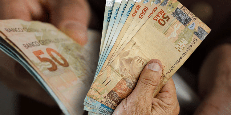 Pessoa contando notas de reais enquanto organiza o orçamento com o pagamento da segunda parcela do 13º salário.