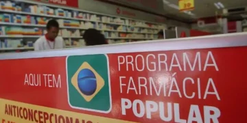 Letreiro do programa Farmácia Popular em farmácia com prateleiras e atendentes ao fundo