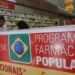 Letreiro do programa Farmácia Popular em farmácia com prateleiras e atendentes ao fundo