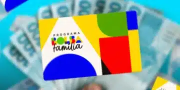 Mão segurando cartão do Programa Bolsa Família com cédulas de dinheiro ao fundo