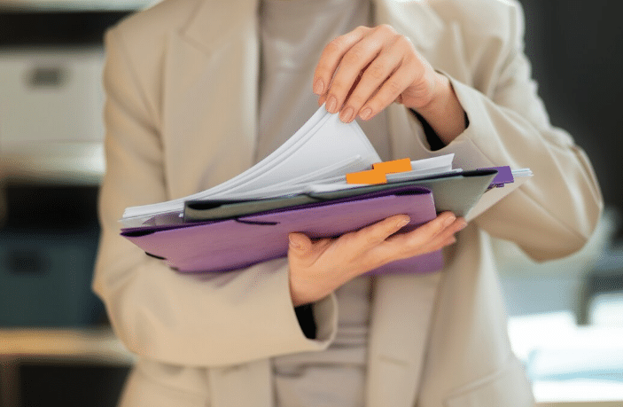 Organização de documentos empresariais com pastas coloridas Pessoa organizando documentos em pastas coloridas dentro de escritório corporativo