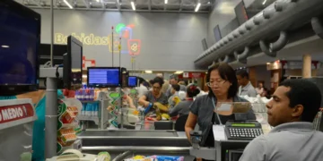 Funcionários e clientes interagem rapidamente nos caixas de supermercado lotado.