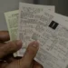 Mão masculina segurando três cupons fiscais variados com informações de compras e valores
